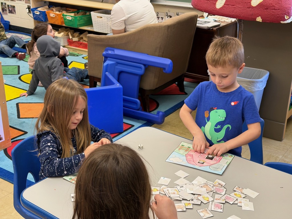 Two students are sitting at a table where they are rolling a dice and velcroing animals to their farm scene. 
