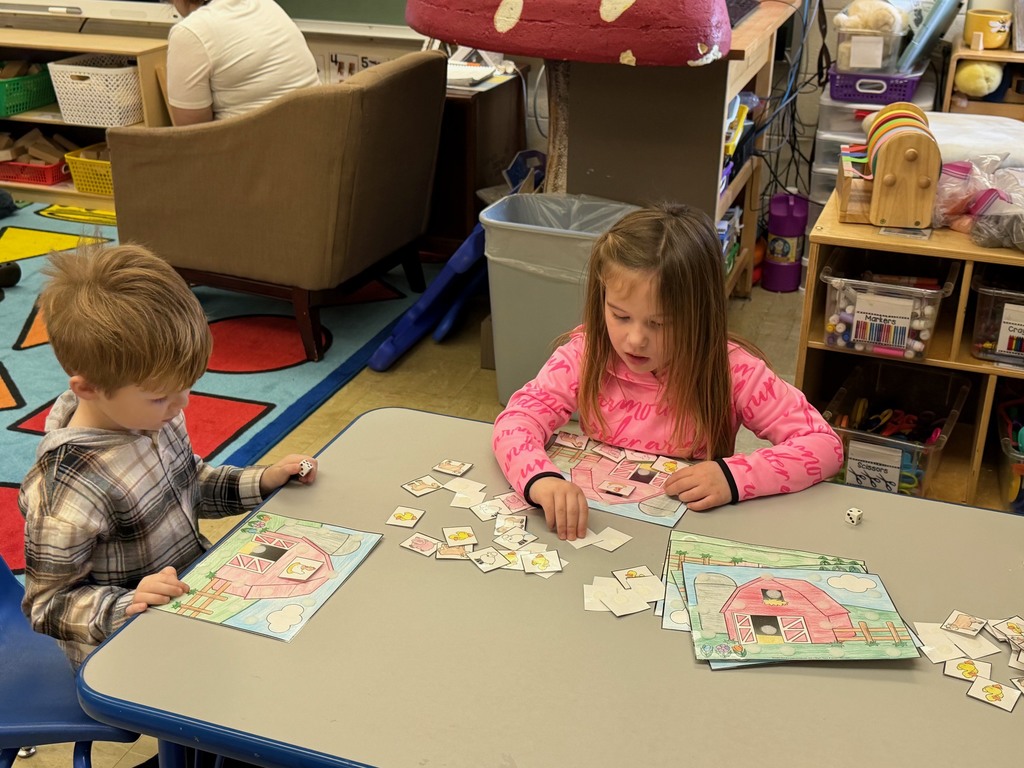 Two students are sitting at a table where they are rolling a dice and velcroing animals to their farm scene. 