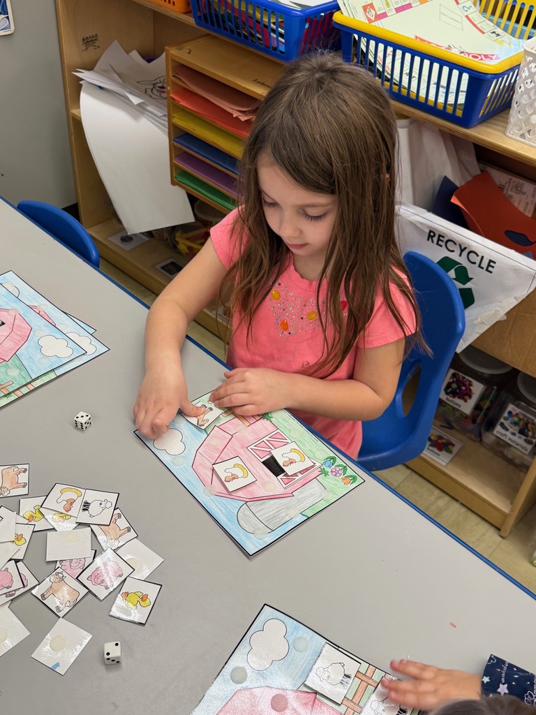 One student is sitting at a table where the student isrolling a dice and velcroing animals to their farm scene. 