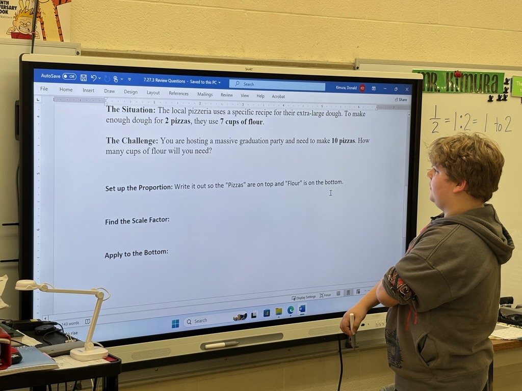 A student is at the white board working out a problem of ratios and proportions. The student is looking at the board reading the problem before starting.