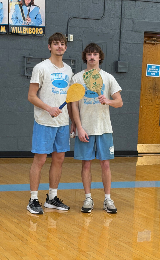 Two students are standing side by side. Each is holding a racket.