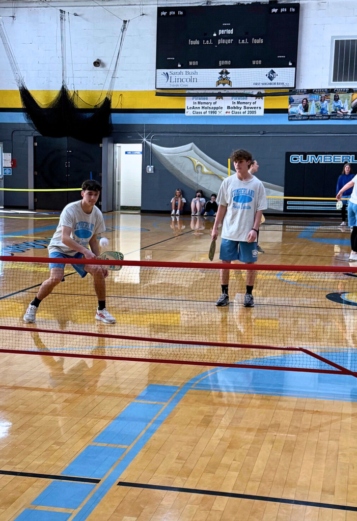 Two students are standingbehind the net. One student is attacking the ball to hit it back over the net. 
