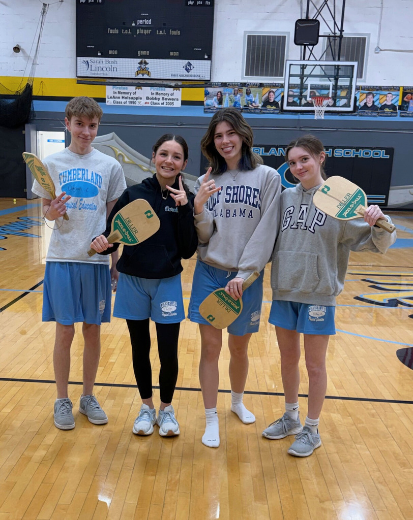 Four students are standing side by side. They all are holding rackets. 