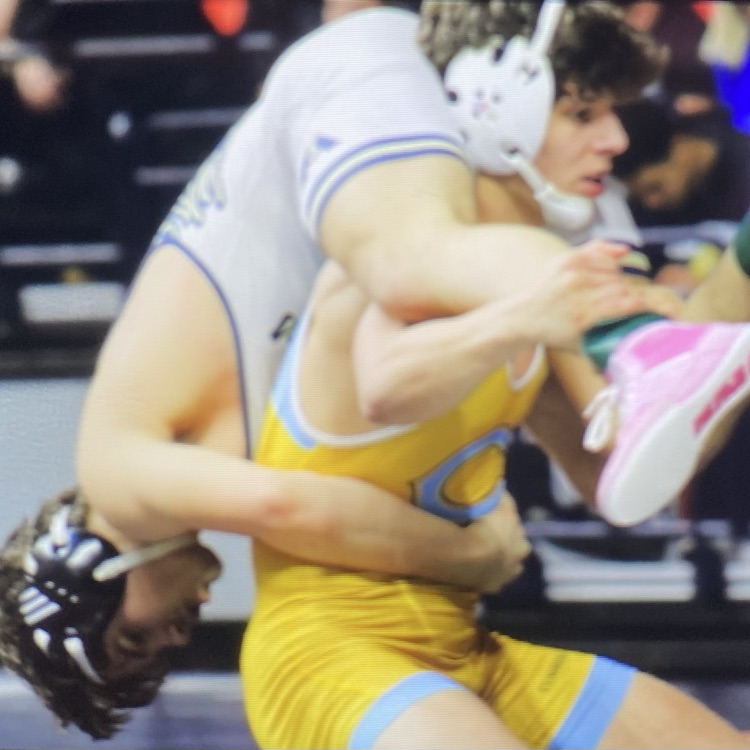 Owen is standing up. He has his opponent on his back. His opponent is upside down and Owen is holding his leg. His opponent has his arms around Owen’s waist.