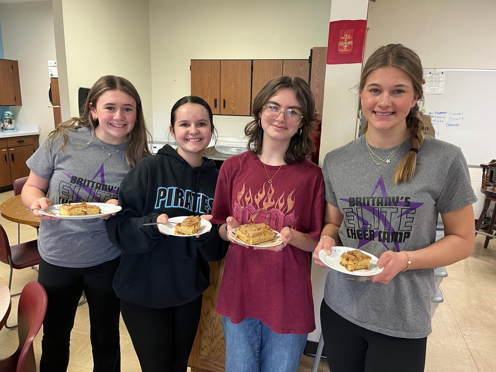 Four students are standing side by side with a plate filled with their coffee cake.