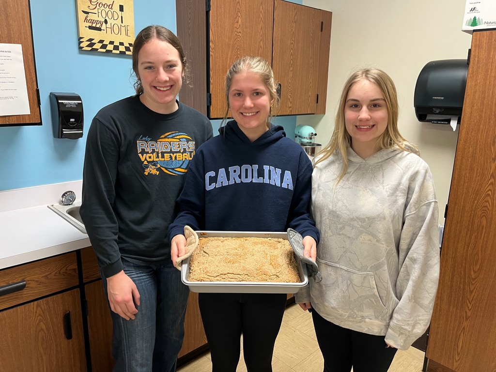 Three students are standing side by side with a pan of their baked coffee cake.