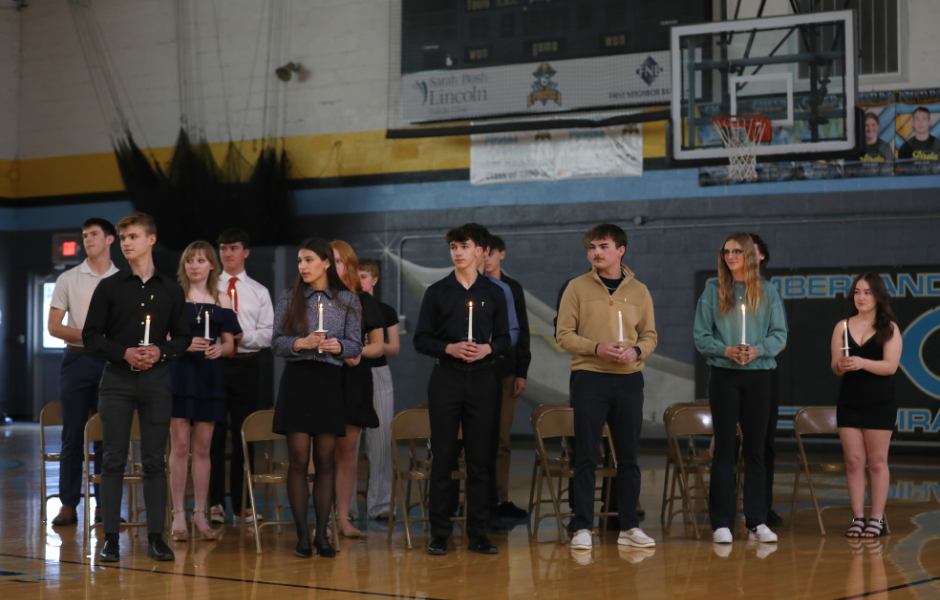 Pictured are 15 new inductees into NHS. They are each standing and holding a lighted candle. They are looking to their right.