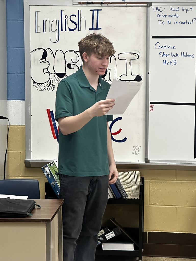 A student is standing and reading from a piece of paper.
