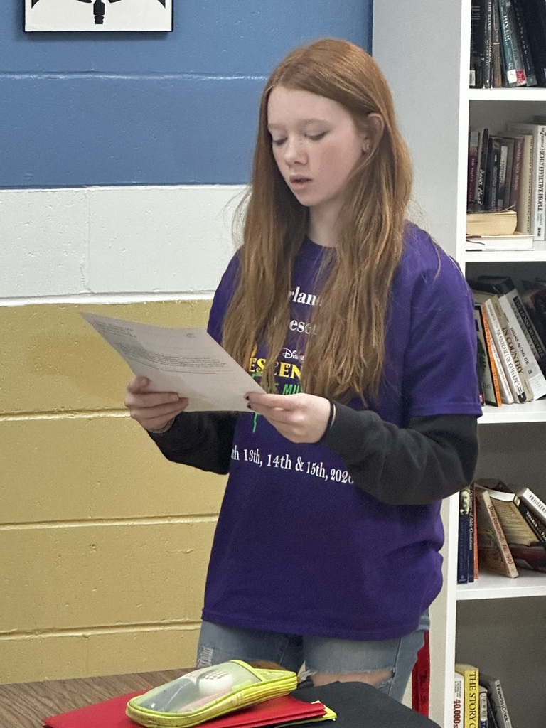 A student is standing and reading from a piece of paper.