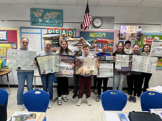 Eleven students are standing in the back of the room holding up brochures that they have received from the parks. 