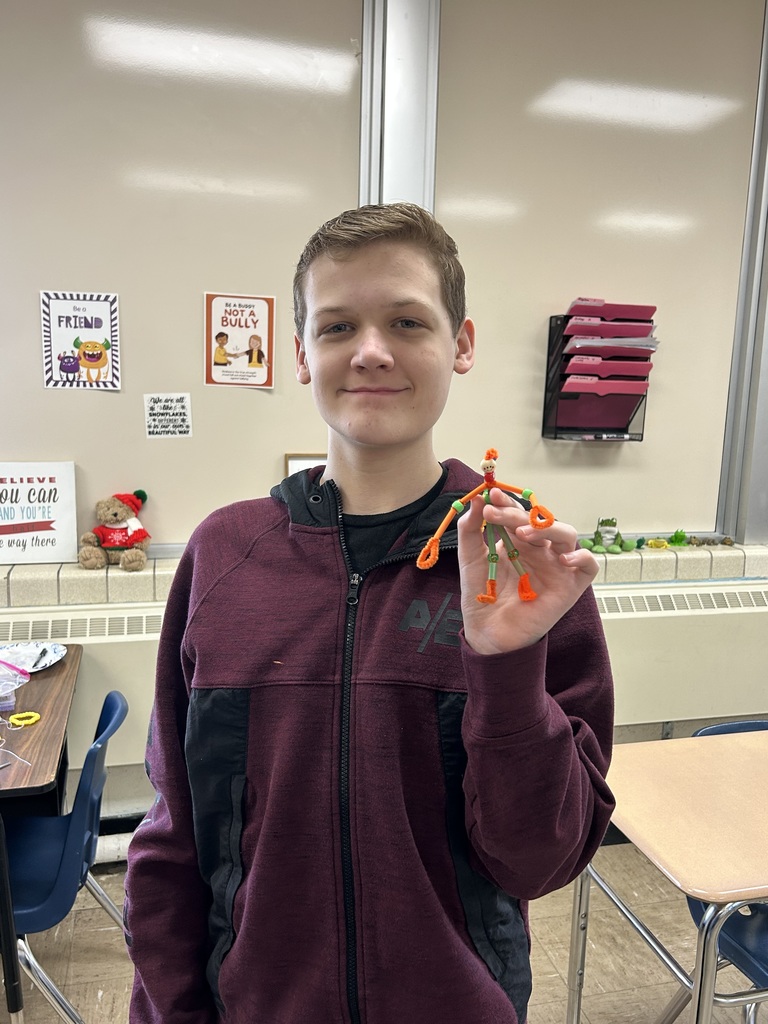 A student is standing and holding his pipecleaner buddy.  It is made from pipecleaners and beads. 