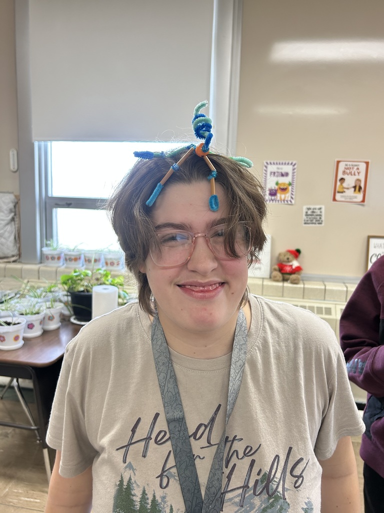 A student is standing and has placed her pipecleaner buddy on her head.  It is made from pipecleaners and beads. 