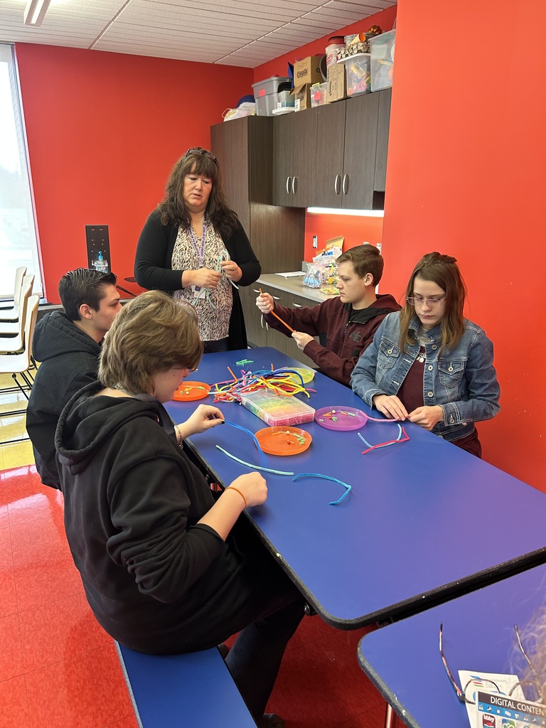 Students are sitting at a table making a buddy with pipecleaners and beads. 