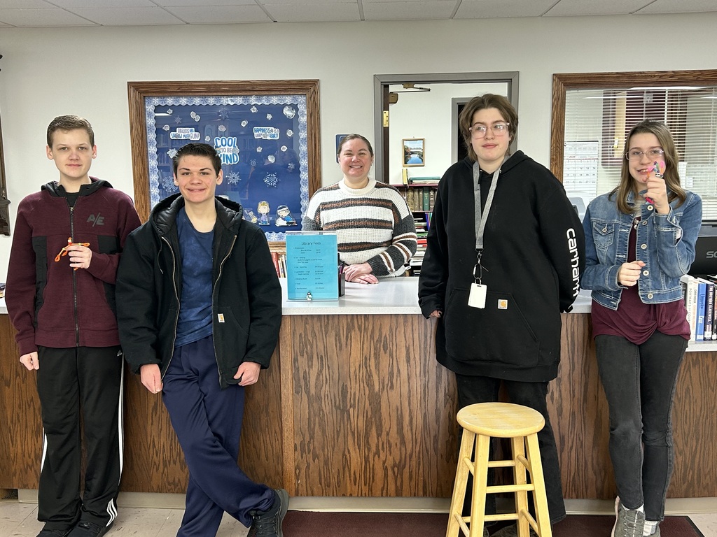 Students are standing at the library checkout counter with the librarian. 