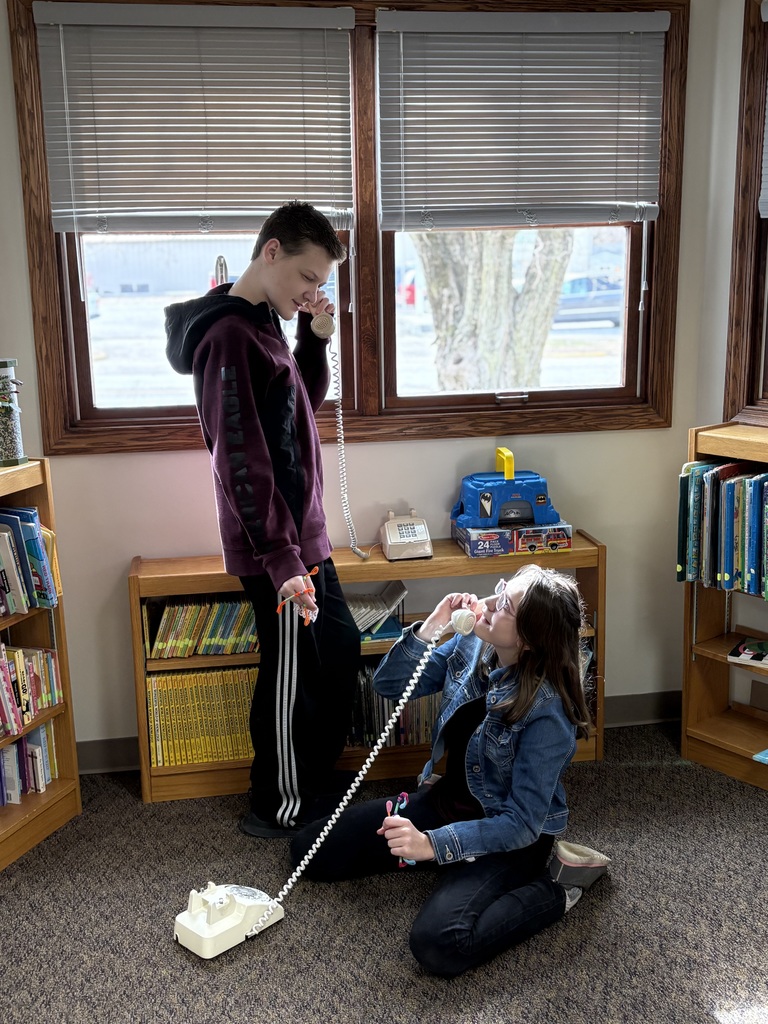 Two students are playing on rotary phones and pretending to call each other. 