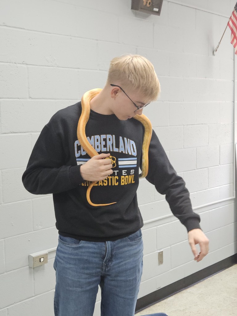 A student is facing the camera. He has Loki the snake hanging from his neck. 