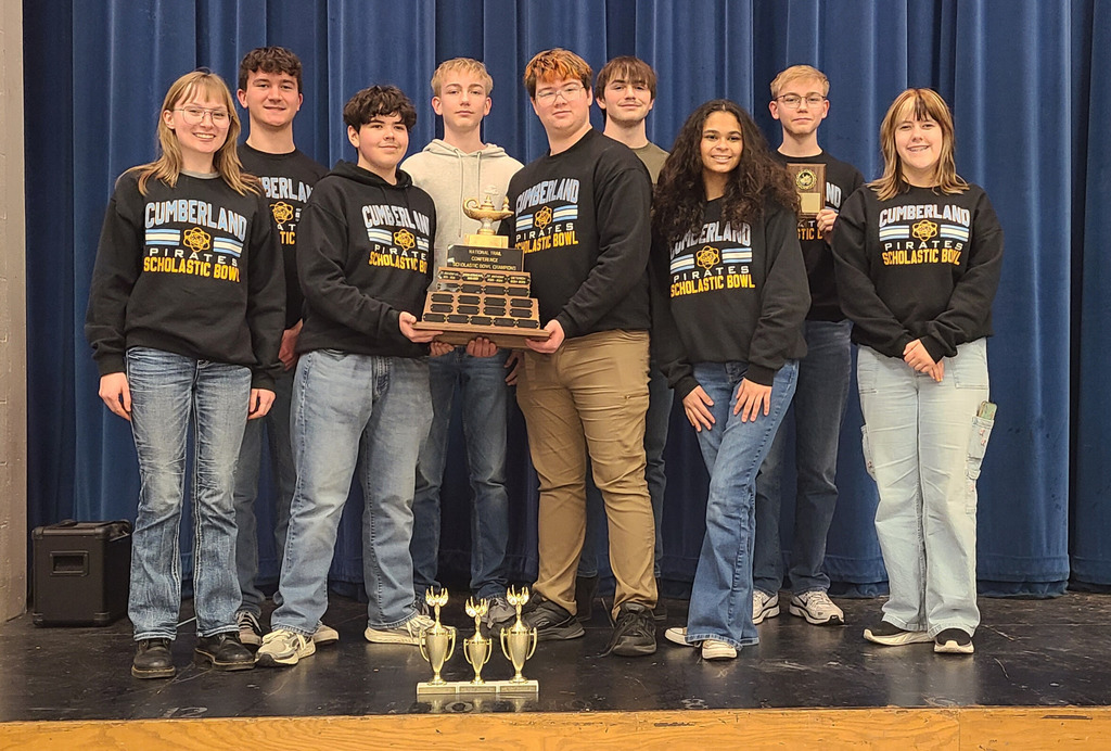 The team is standing on the stage. They are holding the traveling trophy in the center. Their individual tropheys are on the stage in front of them. 