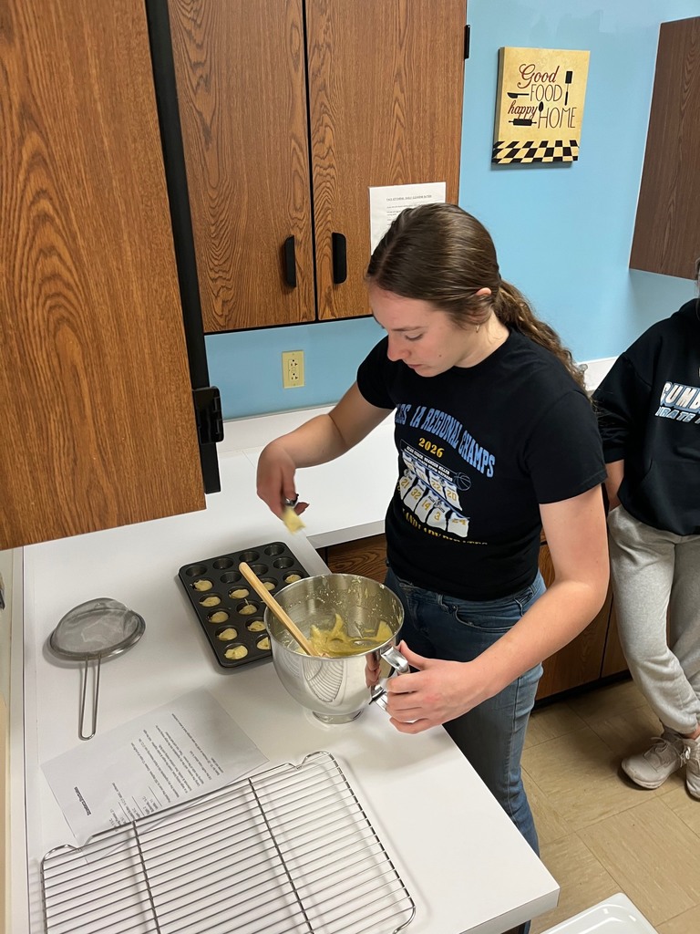 A student is dipping batter from a pan into a mini muffin pan. 