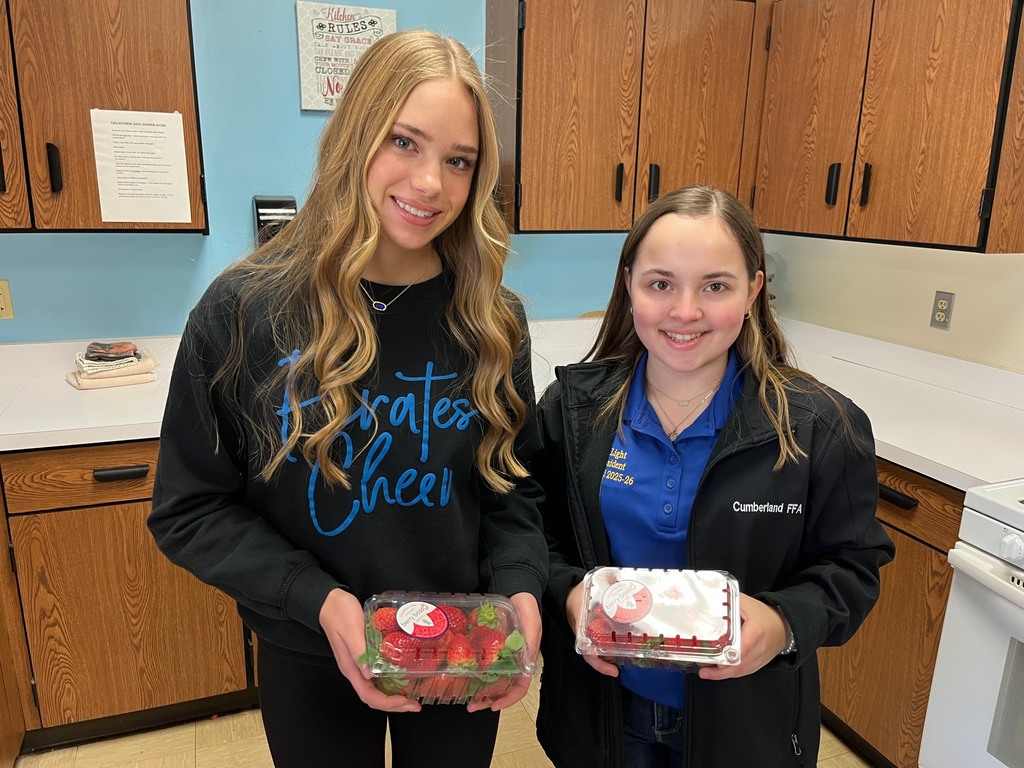 Two students are each holding a container of strawberries. They are standing side by side.