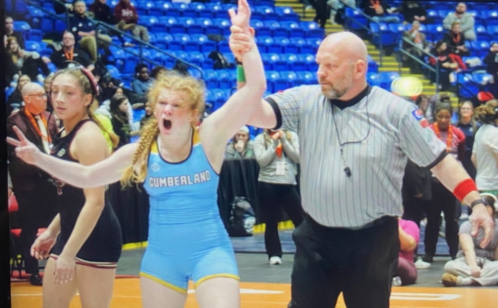 NB's arm has been raised by the referee to signify a win. She is screaming in pure excitement.