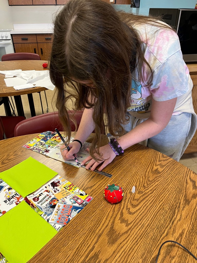 A student is piecing together her pillow project. She is alternating green squares with comic pattern squares.