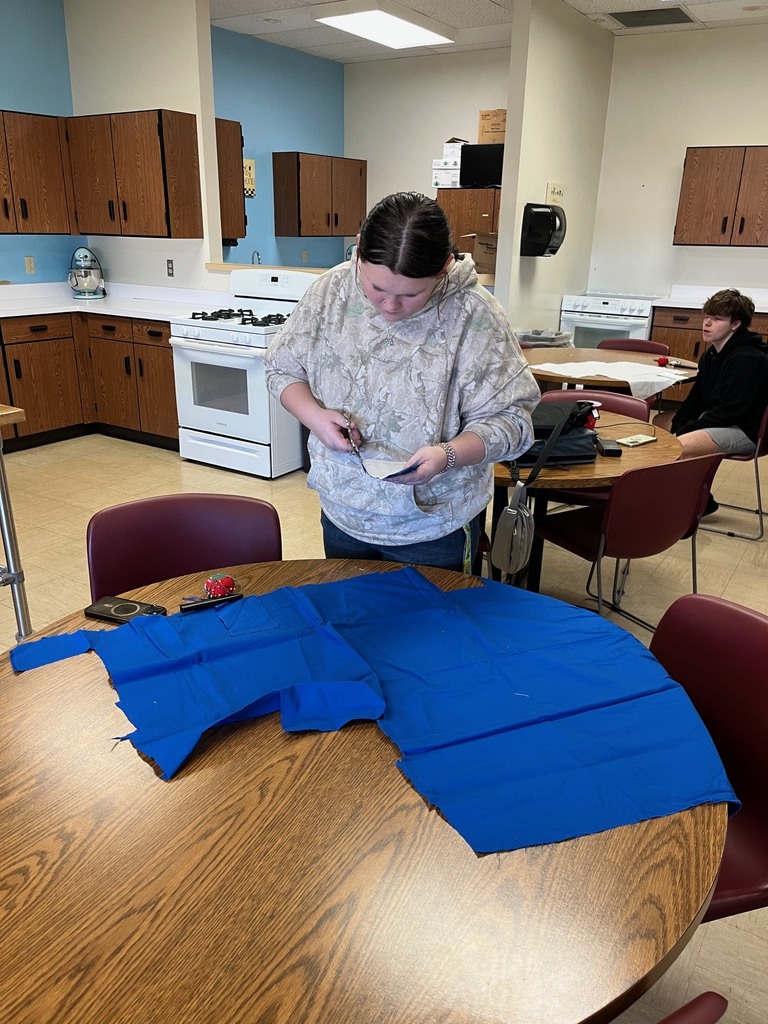 A student is cutting royal blue fabric from a pattern she has layed on top.