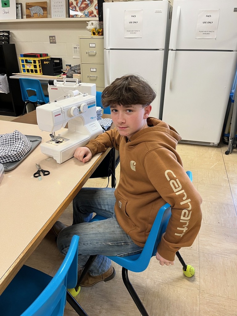 A student is turned around looking at the camera. He was working on the machine to set it up to sew his project.