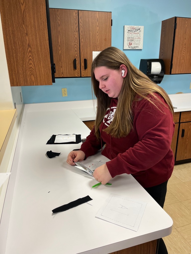 A student is cutting a pattern on fabric with a pair of scissors. The fabric is black.