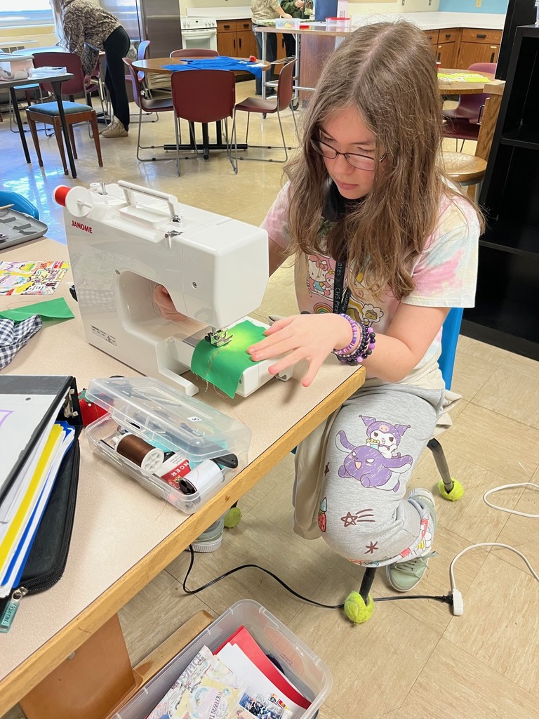 A student is using the machine to sew a seam on a green piece of fabric.
