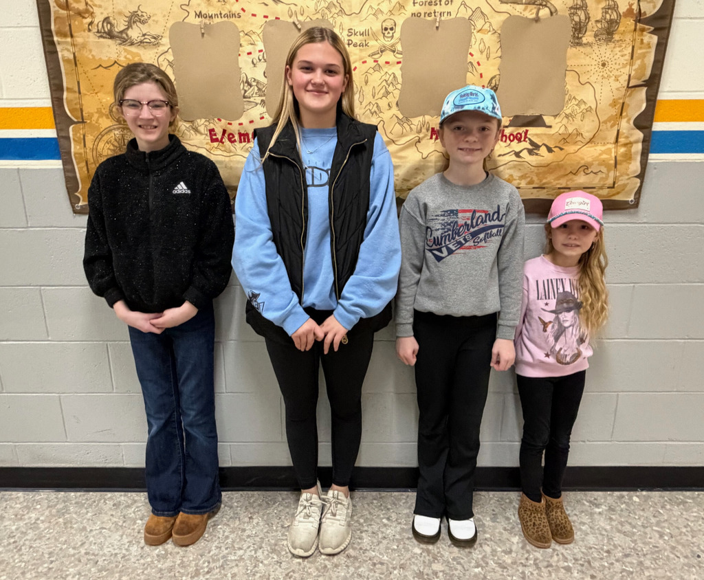 Four students are standing in front of the "Crew of the Month" bulletin board. They are side by side. 