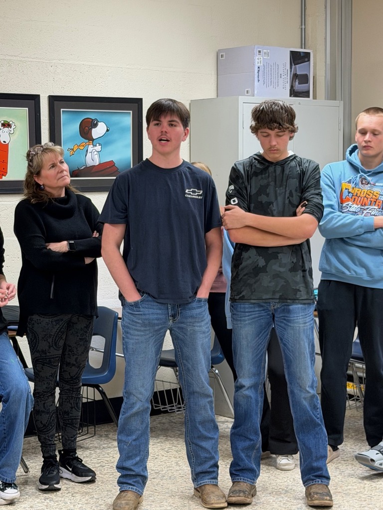Four students and a teacher are standing at the agree wall and one is explaining his opinion. 