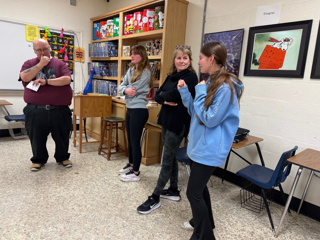 Two students and a teacher are standing at the disagree wall and one is explaining her opinion. 