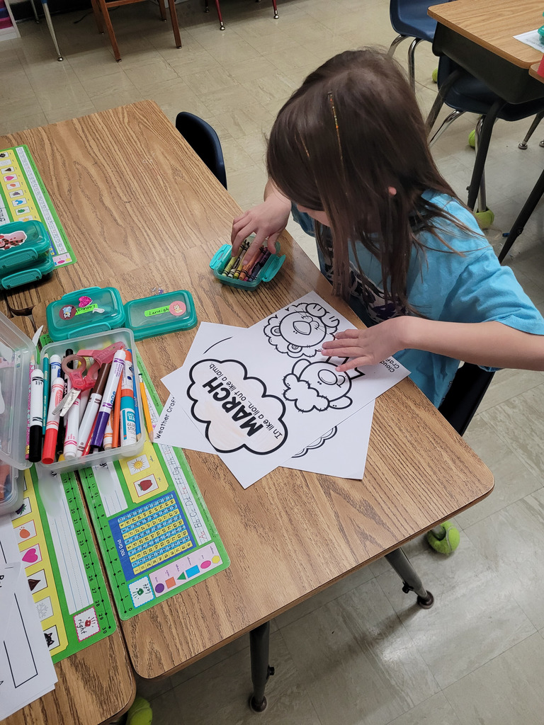 A student is selecting a crayon to color the paper that says March In like a lion...out like a lamb.