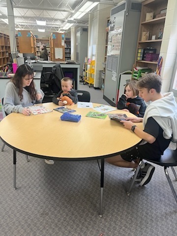 Older students are reading books to younger students. 