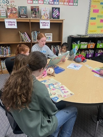 Older students are reading books to younger students. 