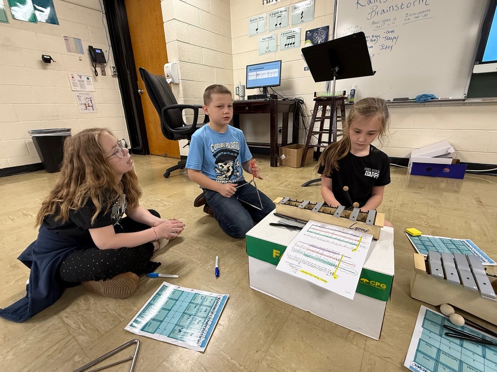 Three students are sitting on the ground and playing an instrument. 