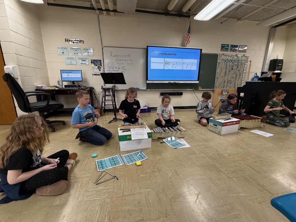 Seven students are sitting on the ground and playing an instrument. 