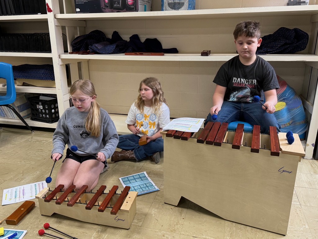 Three students are sitting on the ground and playing an instrument. 