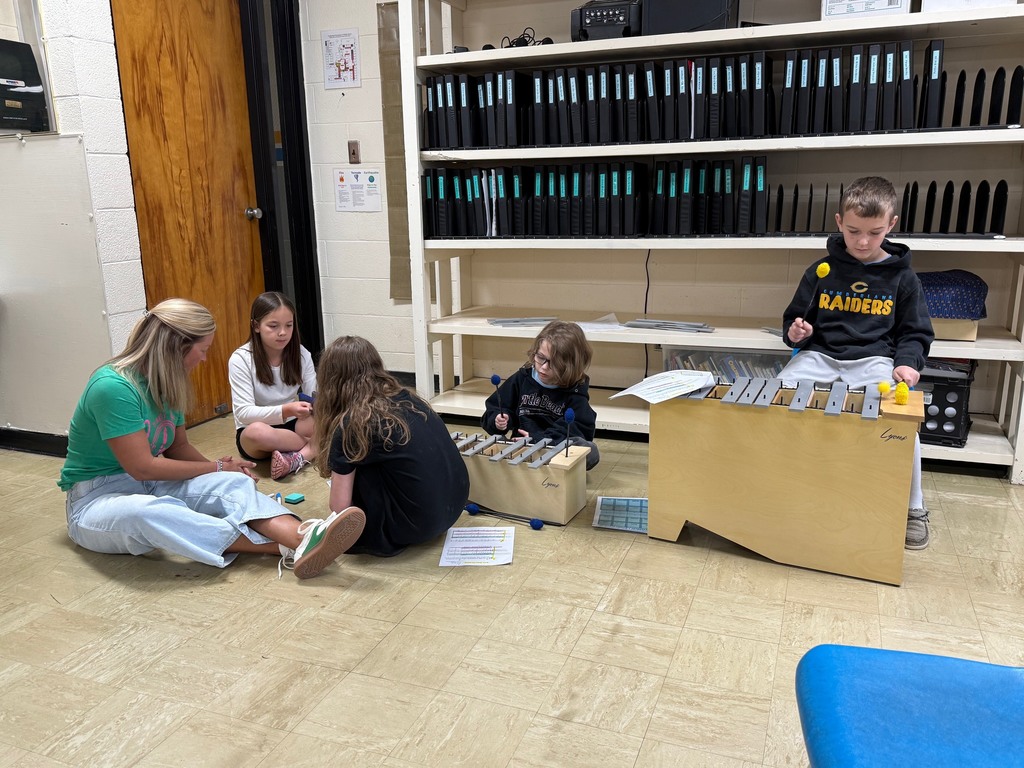 Four students are sitting on the ground and playing an instrument. A teacher is helping a student. 