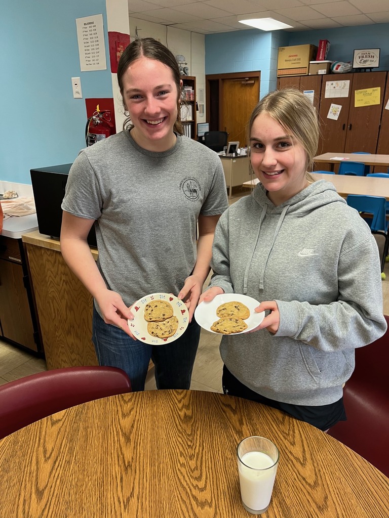 Two students are standing side by side. Each is holding a plate of two cookies. 