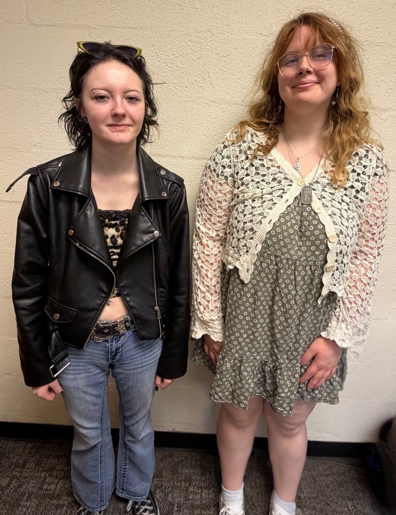 AJ and MC are standing side by side in front of a blank wall.