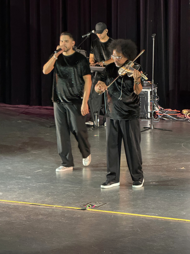Three musicians are performing. One is playing a keyboard, another is playing the violin, and the  third is singing. 