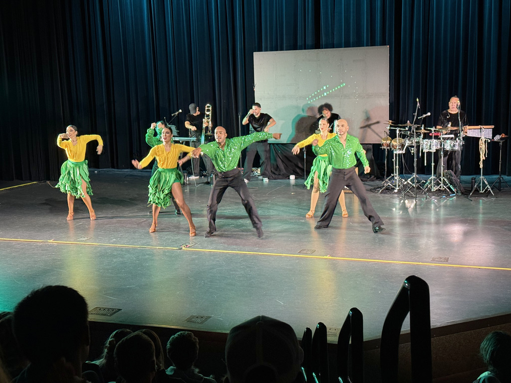 Five dancers are performing. THey are wearing green, yellow and black. They are doing a Spanish style of dance. 