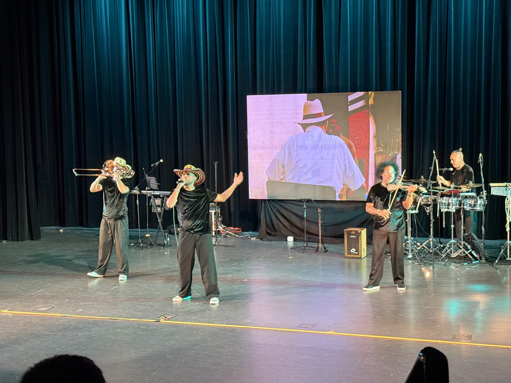 Three musicians are performing. One is playing a trombone, another is playing the violin, and the  third is singing. 