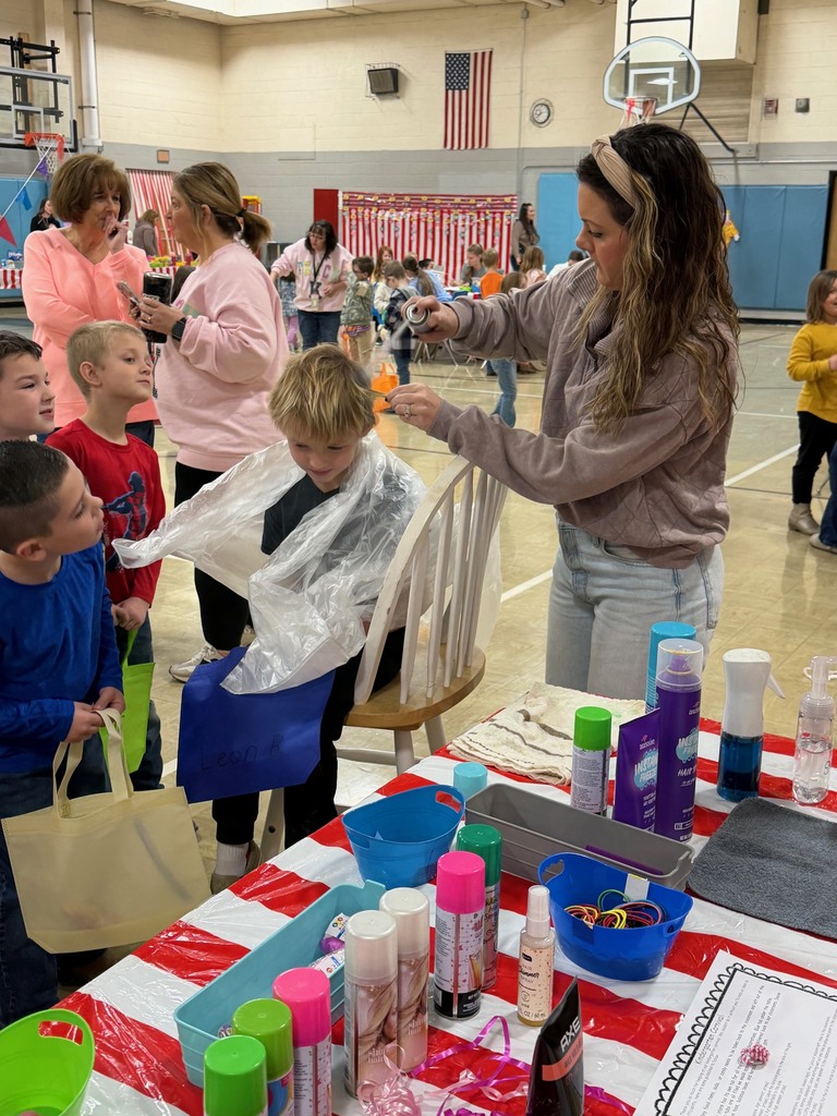 An adult is spraying a students hair blue. 
