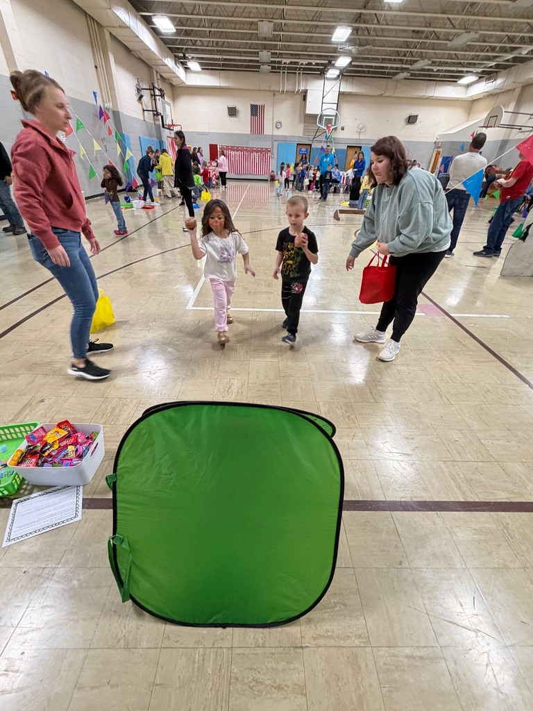Two students are throwing footballs at a green hole. 