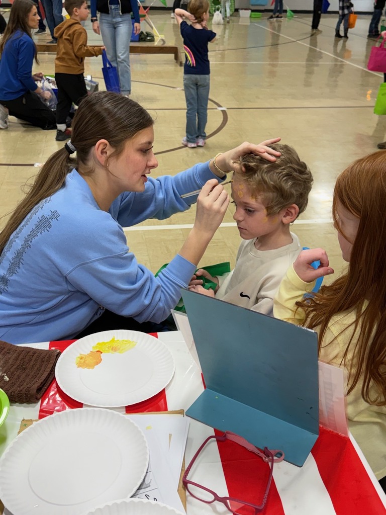 An adult is painting a students face. 