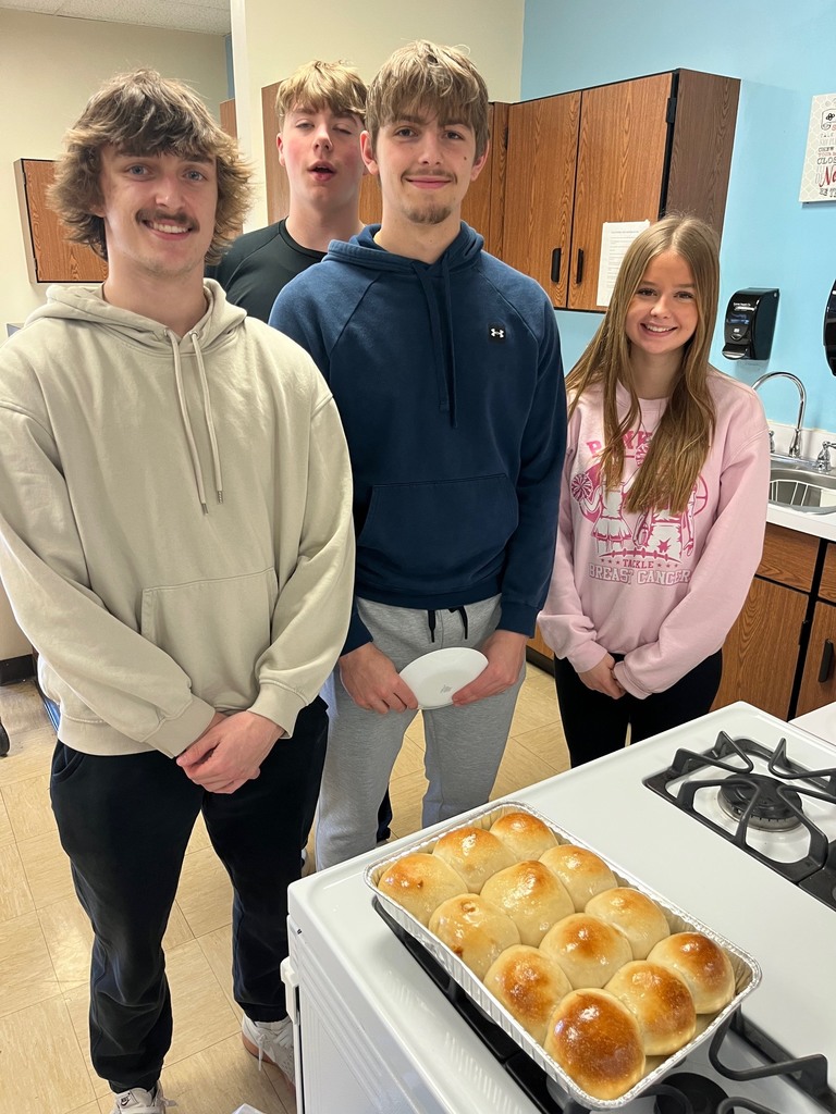 Three students are standing by their pan of baked rolls. 