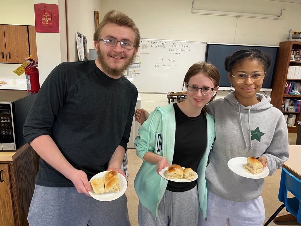 Three students are each holding a plate of rolls. 