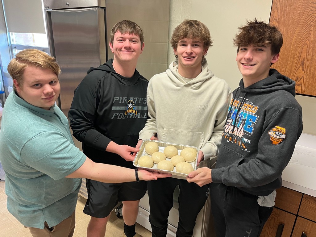 Four students are standing by their pan of unbaked rolls that have risen. 